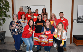 City staff wearing their favorite football team, Kansas City Chiefs gear and carrying a flag inside a building