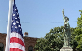 American flag placed in the ground at City Hall with miniature Statue of Liberty in the background