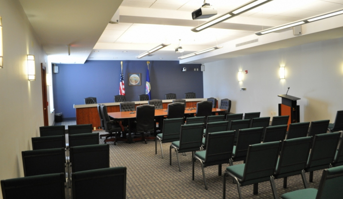 Photo of Commission room with chairs for the public, a podium for the public in front of a desk for elected officials