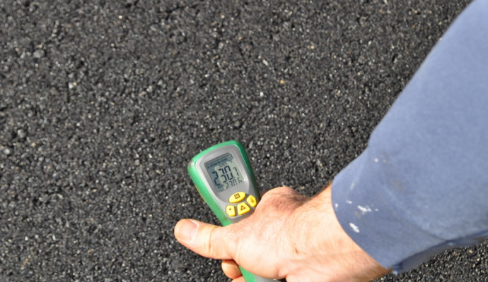 Digital readout of thermometer on recently paved asphalt shows 230.7 degrees Fahrenheit